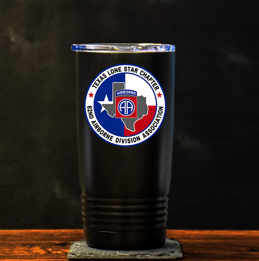 A black insulated tumbler with a clear lid stands on a stone coaster on a wooden surface against a dark background. The tumbler features a circular 'Texas Lone Star Chapter 82nd Airborne Division Association' logo on the front.